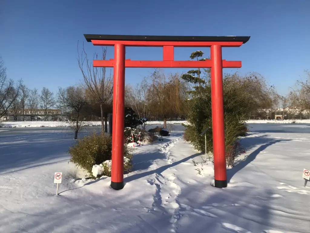 Piros torii kapu egy havas japánkertben, ahol a fehér hó kiemeli a színek kontrasztját